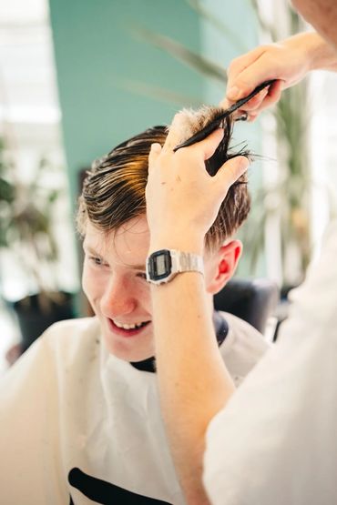 A young man smiling while getting a haircut.