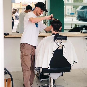 Barber cutting a man's hair in a modern salon with a large mirror.