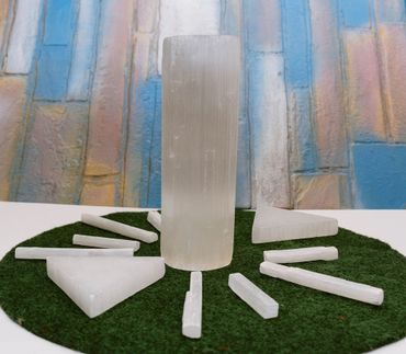 Various pure selenite crystals arranged on green turf with a colorful stone wall background.