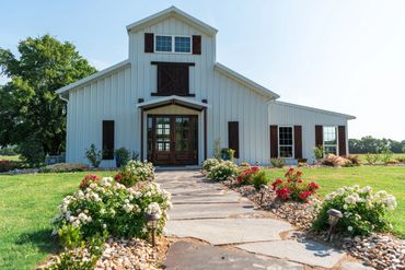 Elegant and rustic white barn venue with stained wood accents with a flagstone path lined with roses