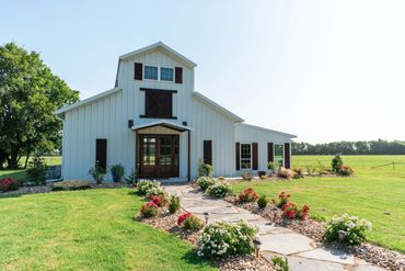 Elegant and rustic white barn venue with stained wood accents sits on a path lined with roses