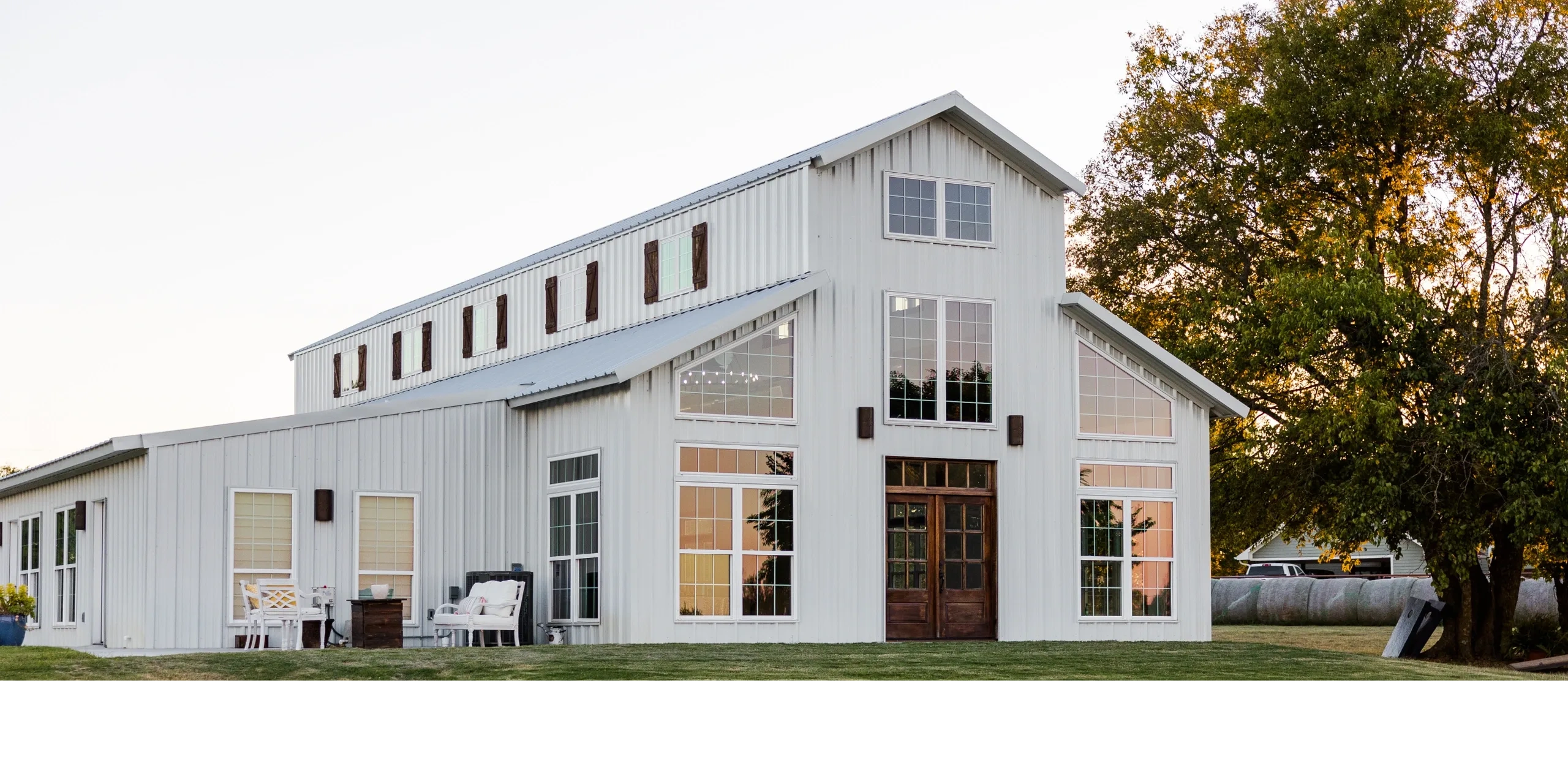 Elegant and rustic white barn venue with stained wood accents and a sunset reflected in the windows