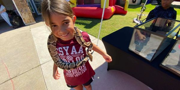 Young girl smiling with snake around her neck.