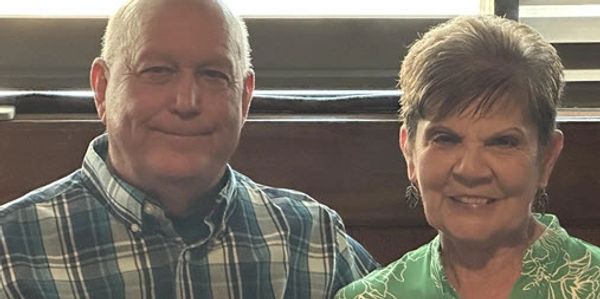 An elderly couple smiling indoors, sitting closely together.