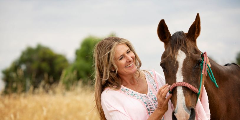A woman smiling while petting a brown horse in a field.