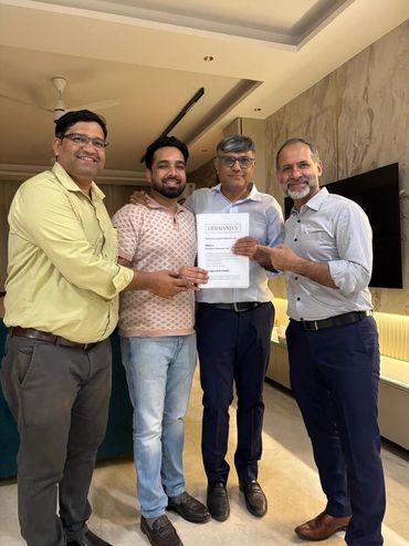 Four men smiling and holding a document titled 'DERMANTY' indoors.