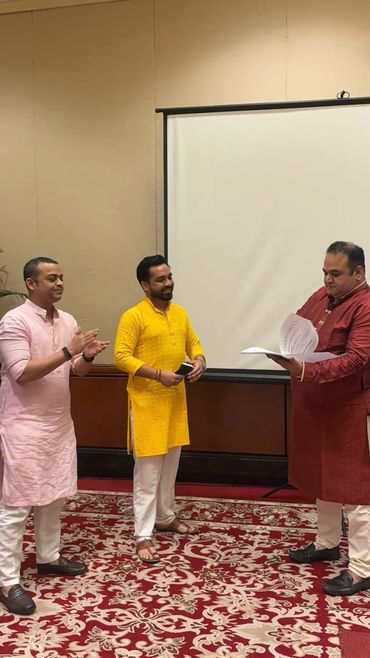 Three men in traditional attire engaging in a formal document exchange.