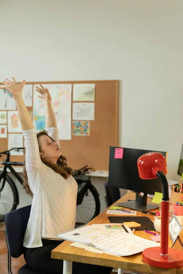 A woman stretching at her work desk in an office environment.