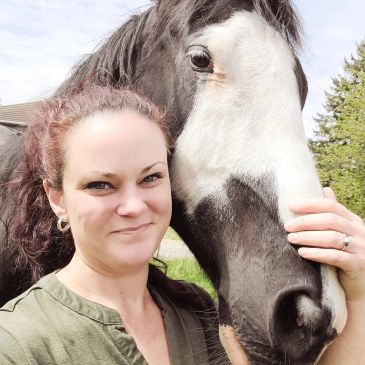 Woman posing with a black and white horse outdoors.