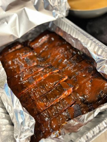 Barbecue ribs covered in rich sauce in an aluminum tray.
