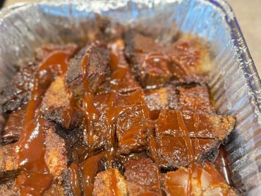 Sliced smoked brisket with barbecue sauce in a foil tray.