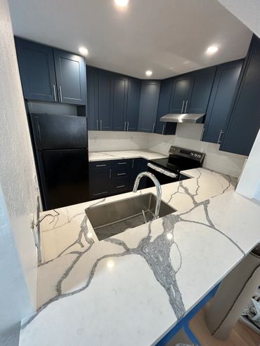Modern kitchen with dark blue cabinets and marble countertops.