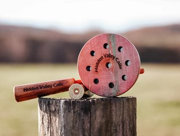 A wooden hunting call labeled 'Hidden Valley Calls' on a tree stump outdoors.