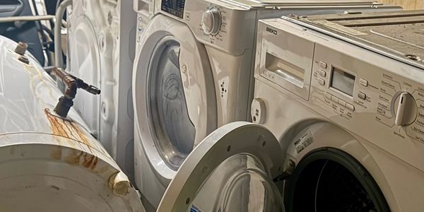 Row of old, dusty washing machines and appliances in storage.