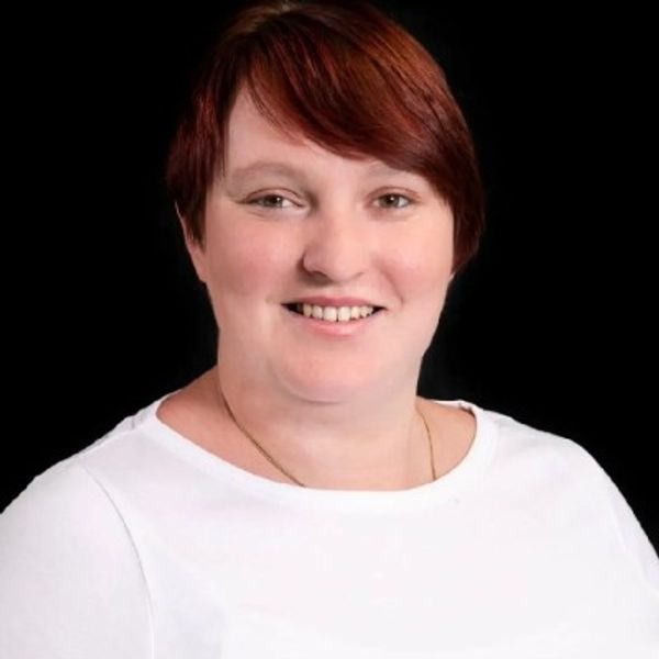 Portrait of a smiling woman with short red hair in a white top.