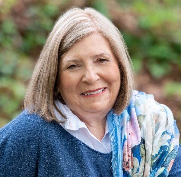 Smiling older woman outdoors in a blue sweater and floral scarf.