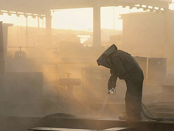 Worker in protective gear spraying in a dusty industrial environment.