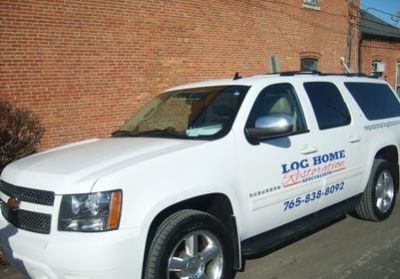 White pickup truck with Log Home Electric signage parked by a brick wall.