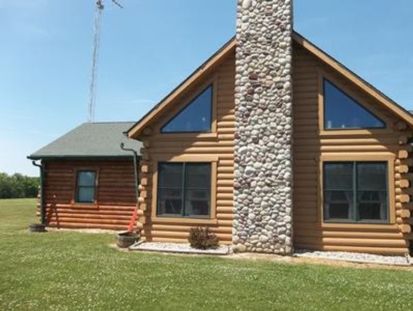 Front view of a log cabin with a stone chimney on a sunny day.