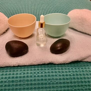 Two bowls, a dropper bottle, and two massage stones on a towel.