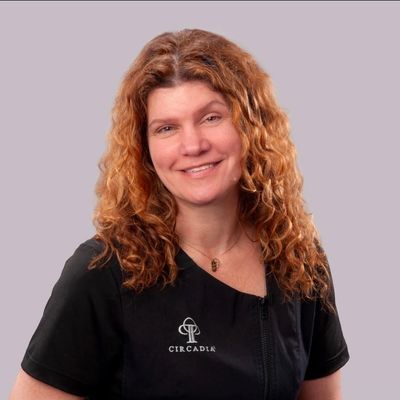 Smiling woman with curly red hair wearing a black Circadia shirt.