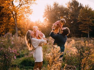 Parents joyfully hold their babies in an autumnal field at sunset.
