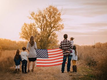 Family holding an American flag outdoors at sunset.