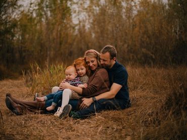 A happy family of four sitting closely together in an autumn field.