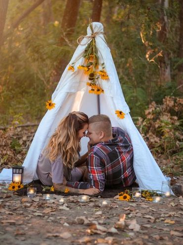 Couple sharing a tender moment inside a decorated white teepee in a forest.