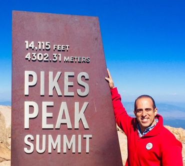 Man smiling next to Pikes Peak Summit sign.