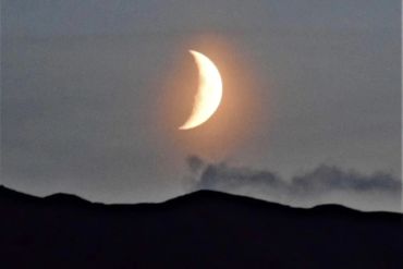 Crescent moon glowing above dark mountains.