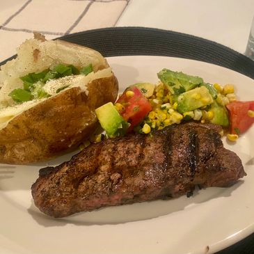 Grilled steak with baked potato and fresh vegetable salad on a white plate.