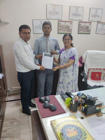 Three people holding a certificate in an office setting with awards on the wall.