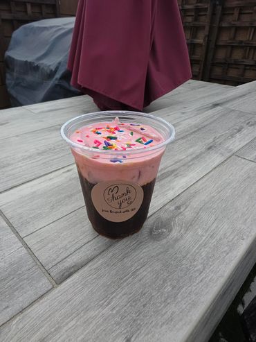 Iced coffee with pink cream and colorful sprinkles in a plastic cup.