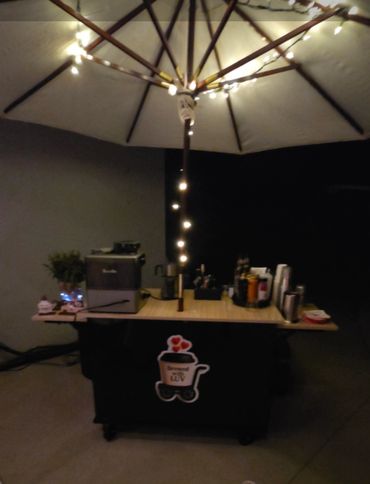 A cozy coffee cart with umbrella and string lights at night.