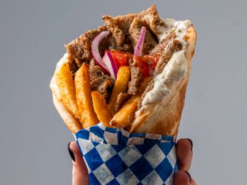 Hand holding a loaded gyro wrap with fries and meat.