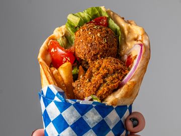 Hand holding a falafel wrap with vegetables.