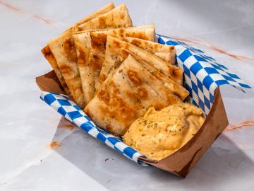 Grilled pita bread with hummus dip in a food tray.
