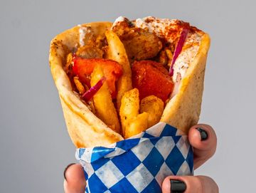 Hand holding a wrapped kebab with fries and chicken.