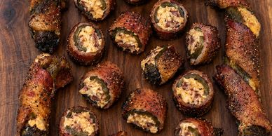 Bacon-wrapped, stuffed jalapeños on wooden board.