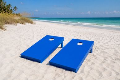 Two blue cornhole boards set up on a sandy beach.