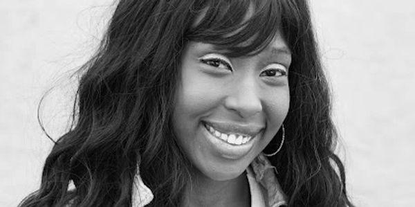 Smiling woman with long wavy hair wearing a denim jacket and white top.