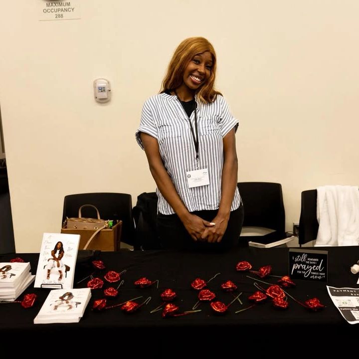 Woman smiling behind a book signing table with red roses.