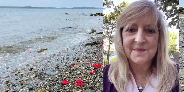 Woman taking a selfie at a rocky beach with scattered red petals on the shore.