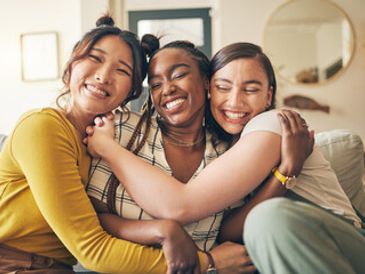 Three friends happily hugging each other indoors.