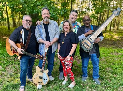 A happy group of five musicians posing outdoors with their guitars.