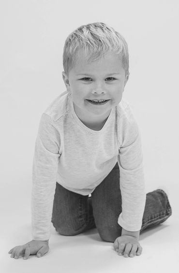 Smiling young boy kneeling on the floor in a casual outfit.