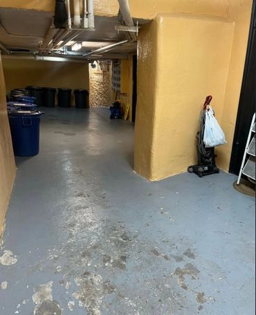 Dimly lit basement corridor with trash bins and a vacuum cleaner.
