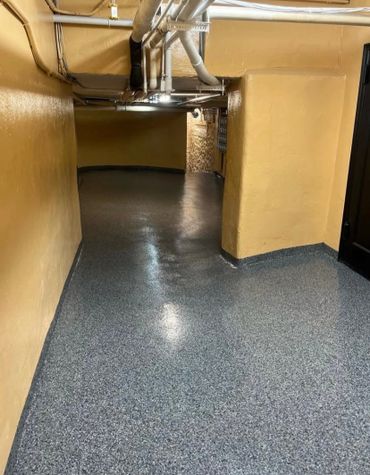 Empty basement hallway with yellow walls and exposed pipes.