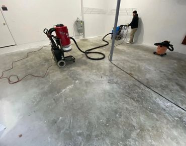 Man using floor polishing machine on concrete floor in empty room.
